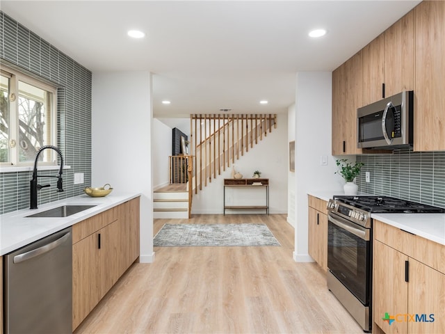 kitchen with a sink, light countertops, appliances with stainless steel finishes, light wood-type flooring, and decorative backsplash