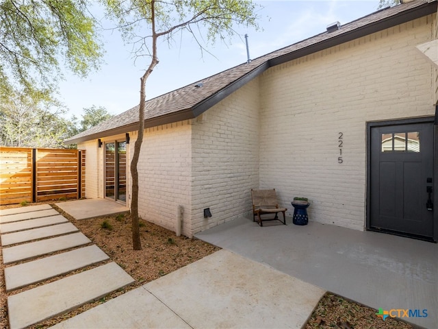 exterior space featuring roof with shingles, brick siding, a patio, and fence