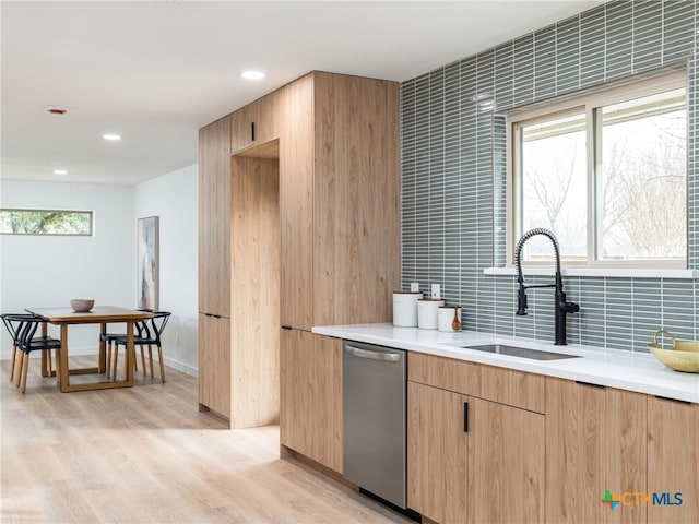 kitchen with backsplash, light countertops, light wood-type flooring, stainless steel dishwasher, and a sink