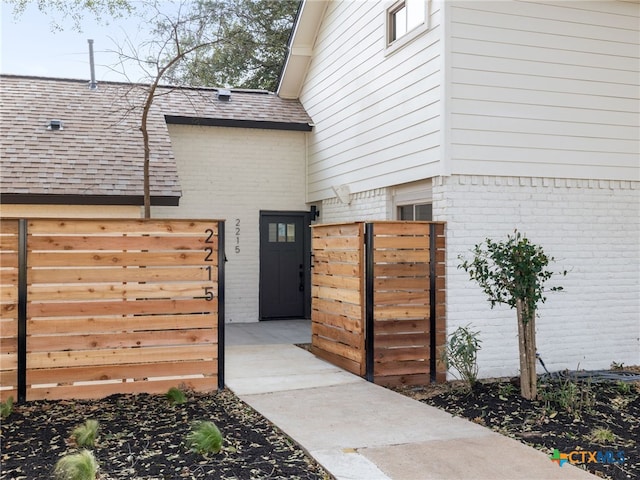 exterior space with brick siding, fence, and roof with shingles