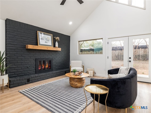 living area with ceiling fan, high vaulted ceiling, wood finished floors, french doors, and a brick fireplace