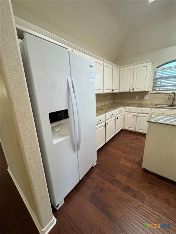 kitchen with white cabinets, decorative backsplash, dark wood finished floors, white fridge with ice dispenser, and a sink