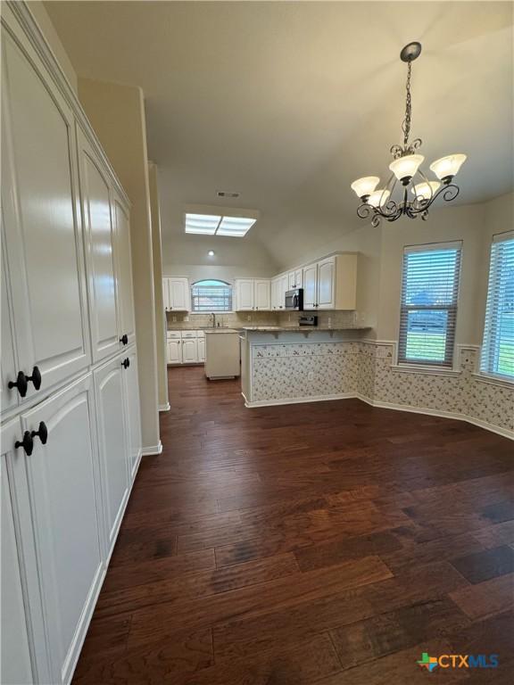 kitchen featuring dark wood-style floors, pendant lighting, an inviting chandelier, white cabinets, and a peninsula