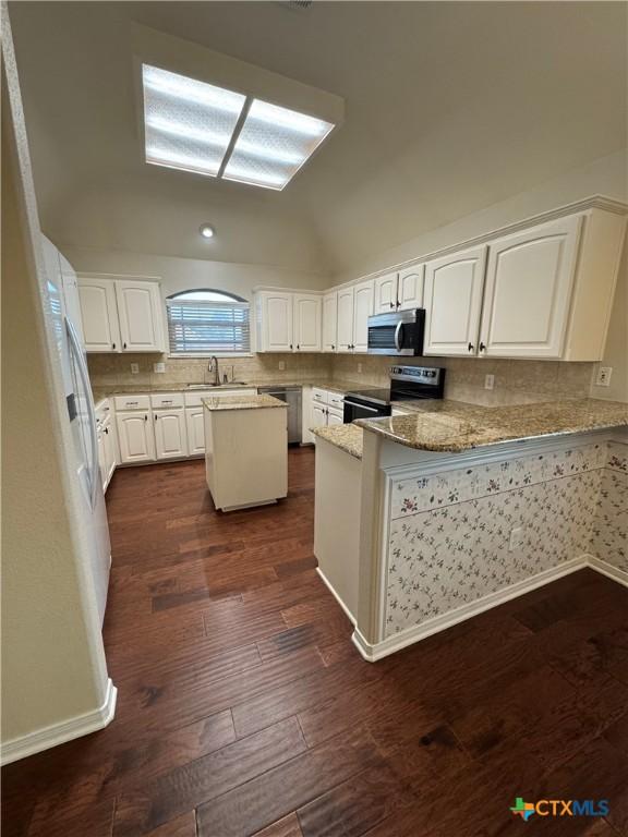 kitchen with lofted ceiling, appliances with stainless steel finishes, dark wood-style flooring, a peninsula, and white cabinetry