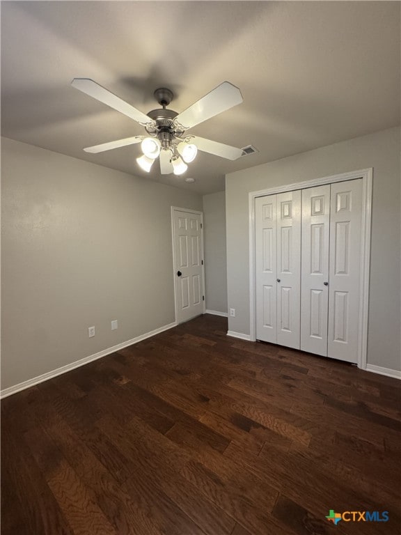 unfurnished bedroom featuring baseboards, visible vents, dark wood finished floors, ceiling fan, and a closet