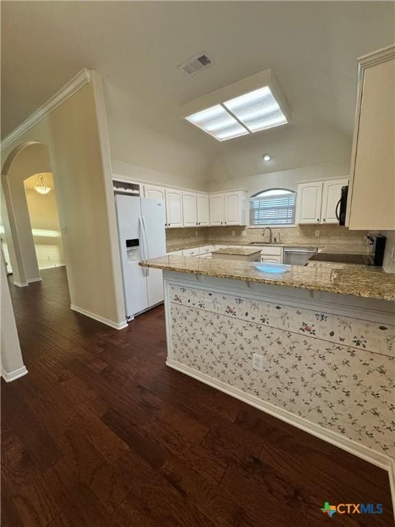 kitchen featuring light stone counters, arched walkways, dark wood finished floors, visible vents, and white fridge with ice dispenser