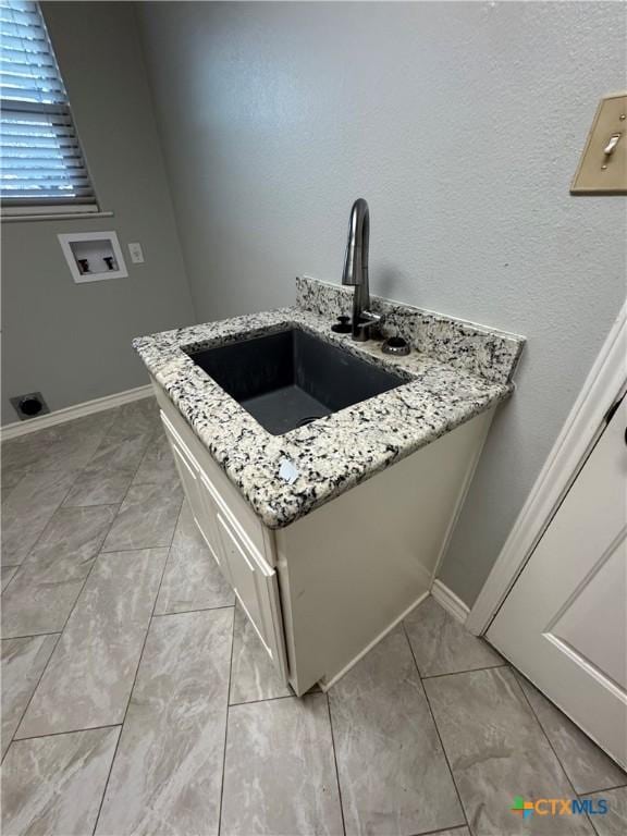 interior space featuring baseboards, a sink, and light stone countertops