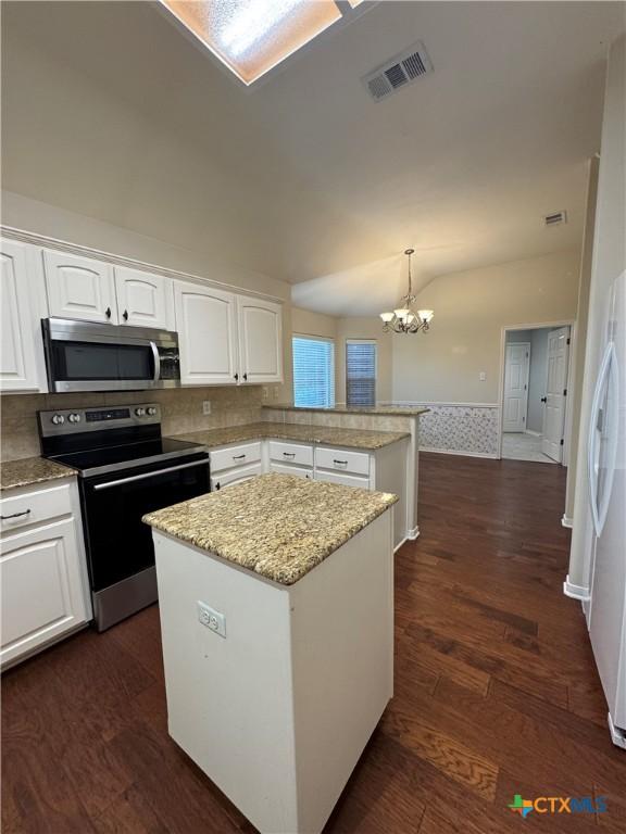 kitchen featuring lofted ceiling, visible vents, appliances with stainless steel finishes, a kitchen island, and a peninsula