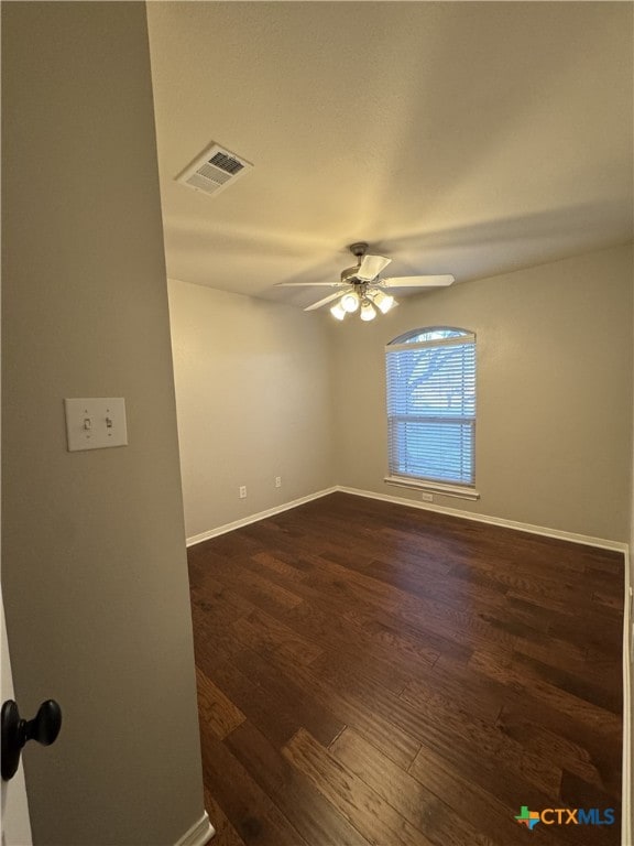 spare room with dark wood-style floors, a ceiling fan, visible vents, and baseboards