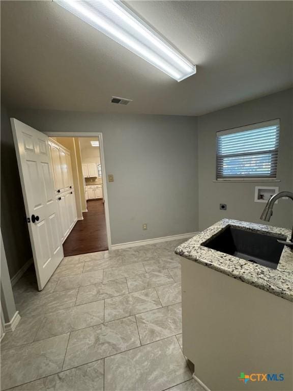 kitchen featuring light stone counters, a sink, visible vents, and baseboards