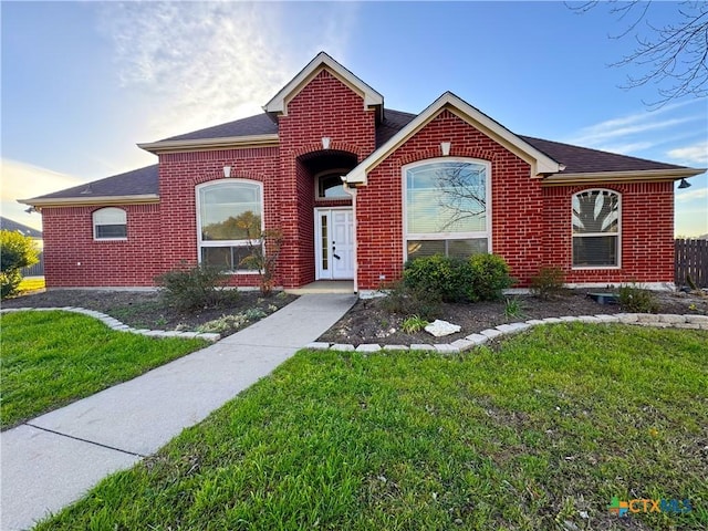 view of front of house featuring a front yard, brick siding, and roof with shingles