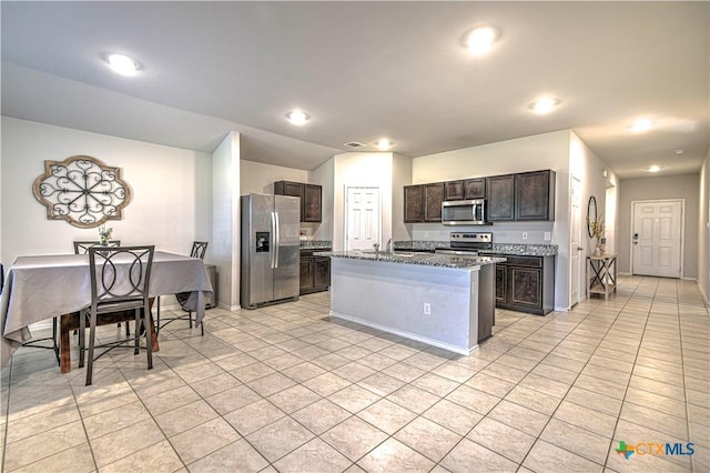 kitchen with dark brown cabinets, a center island, light tile patterned floors, stone counters, and stainless steel appliances