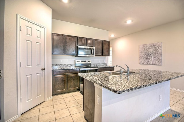 kitchen with a sink, dark stone counters, appliances with stainless steel finishes, light tile patterned floors, and dark brown cabinets