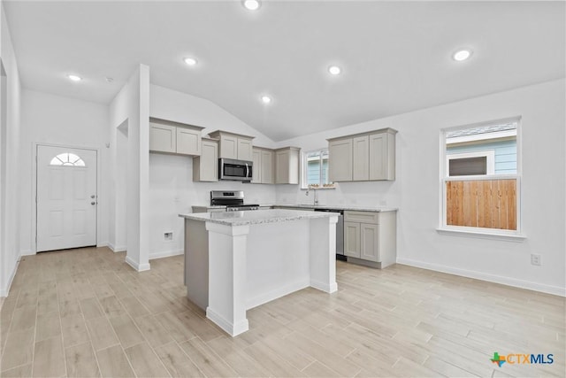 kitchen featuring gray cabinetry, light stone counters, lofted ceiling, a kitchen island, and appliances with stainless steel finishes