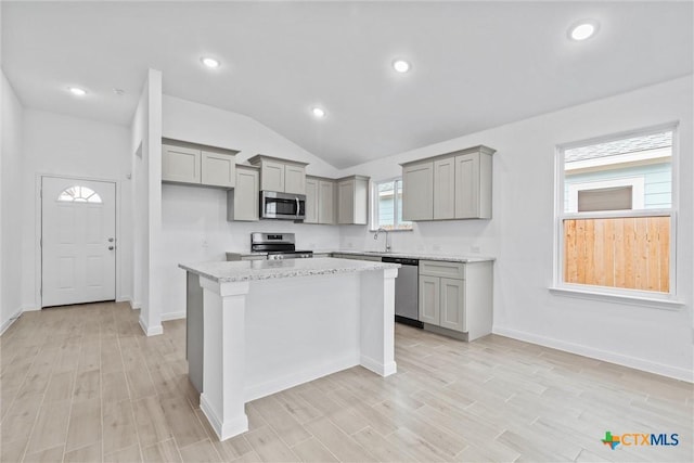 kitchen featuring gray cabinetry, light stone countertops, a center island, stainless steel appliances, and lofted ceiling