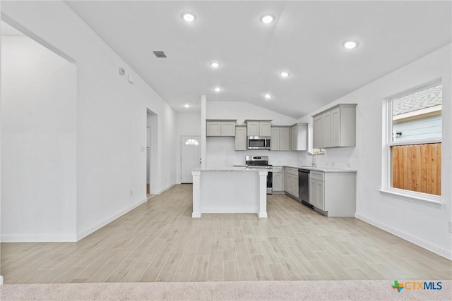 kitchen featuring appliances with stainless steel finishes, light stone counters, gray cabinetry, a center island, and lofted ceiling