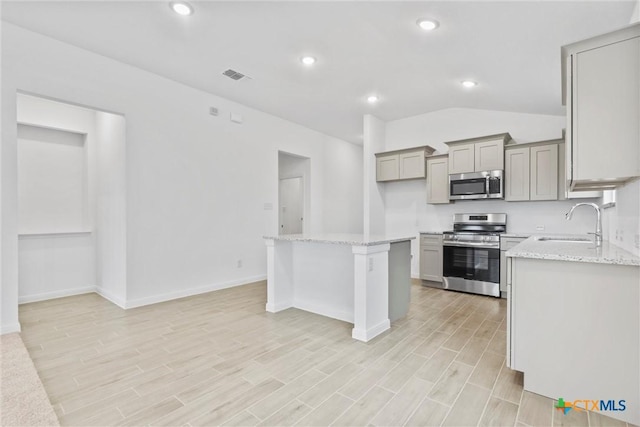 kitchen featuring light stone counters, stainless steel appliances, sink, a center island, and gray cabinets