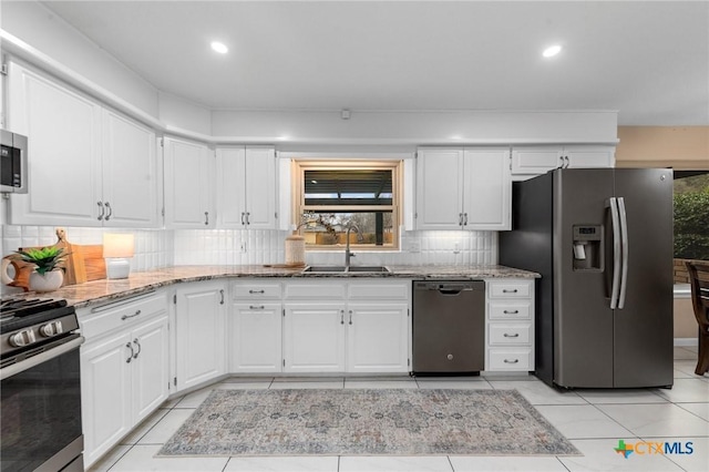 kitchen featuring appliances with stainless steel finishes, sink, white cabinets, backsplash, and light tile patterned floors