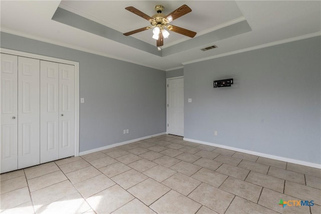 unfurnished bedroom featuring a tray ceiling, ceiling fan, crown molding, light tile patterned floors, and a closet