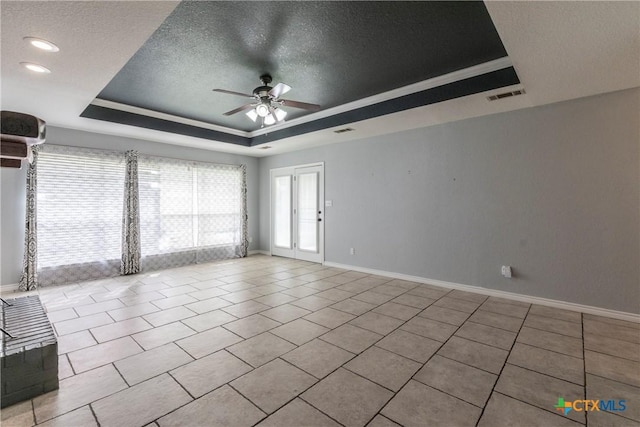 empty room with a tray ceiling, ceiling fan, light tile patterned flooring, and a textured ceiling