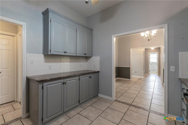 kitchen featuring backsplash, gray cabinetry, light tile patterned floors, and a chandelier