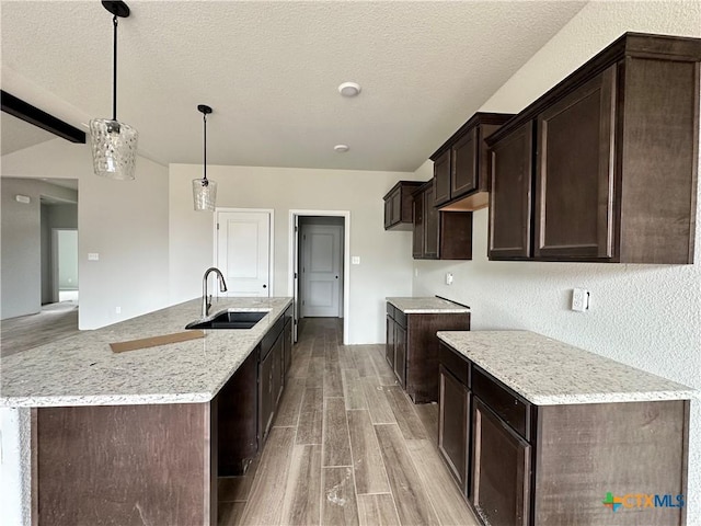 2571 Cedar Glen Dr, Belton, TX 76513 - kitchen featuring light wood-style flooring, dark brown cabinets, an island with sink, light stone counters, and decorative light fixtures