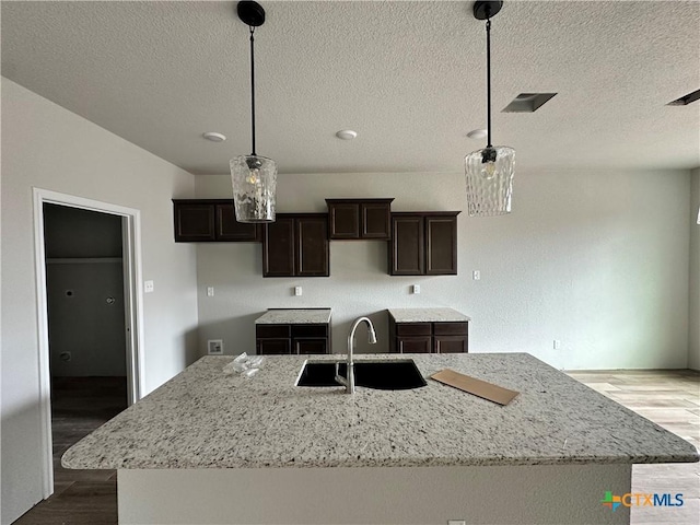 2571 Cedar Glen Dr, Belton, TX 76513 - kitchen featuring an island with sink, wood finished floors, dark brown cabinetry, a textured ceiling, and light stone countertops