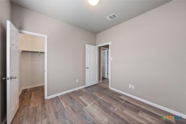 unfurnished bedroom featuring baseboards, visible vents, wood finished floors, a walk in closet, and a closet