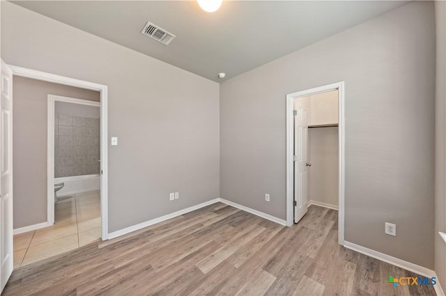 unfurnished bedroom with light wood-style flooring, a spacious closet, visible vents, and baseboards