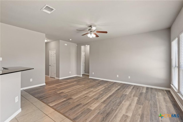 spare room featuring a ceiling fan, visible vents, baseboards, and wood finished floors