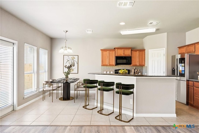 kitchen with black microwave, stainless steel fridge, visible vents, and light tile patterned floors