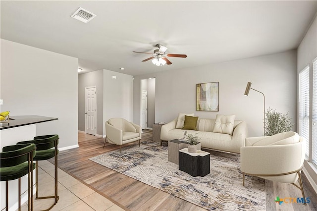 living room with ceiling fan, light wood-style flooring, visible vents, and baseboards