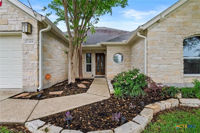 doorway to property with stone siding, a shingled roof, and an attached garage
