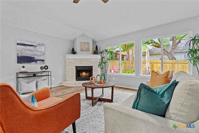 living area with wood finished floors, a ceiling fan, a stone fireplace, and lofted ceiling