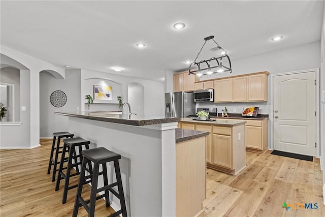kitchen featuring stainless steel appliances, a kitchen breakfast bar, an island with sink, and light brown cabinetry