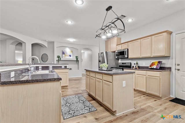 kitchen featuring arched walkways, light brown cabinetry, a center island, and appliances with stainless steel finishes