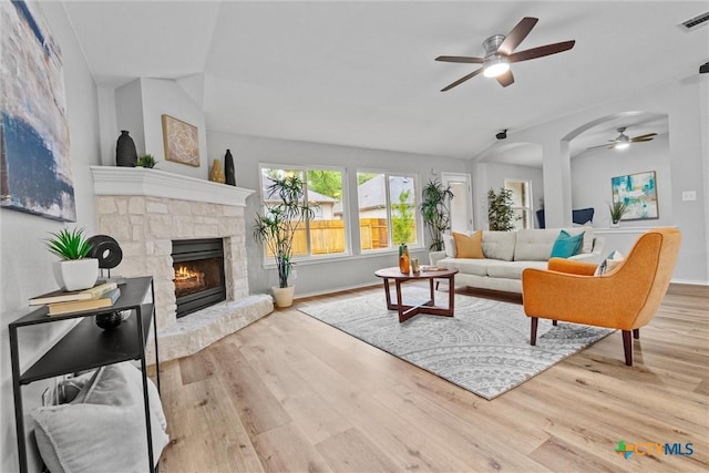 living area featuring a stone fireplace, wood finished floors, lofted ceiling, and ceiling fan