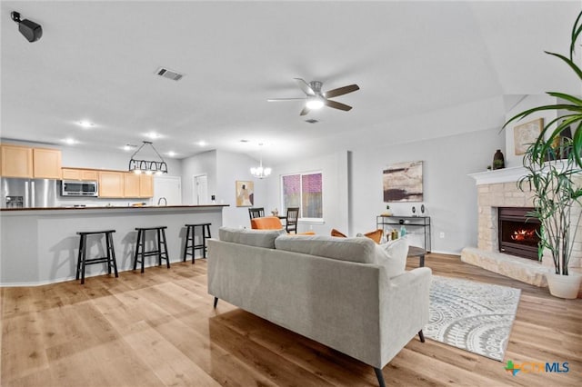living room featuring recessed lighting, visible vents, ceiling fan with notable chandelier, a fireplace, and light wood-type flooring