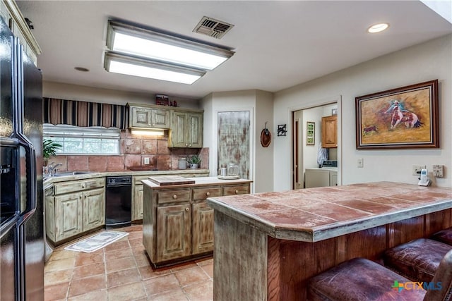 10767 Rosemar Ln, Adkins, TX 78101 - kitchen featuring washing machine and clothes dryer, freestanding refrigerator, a breakfast bar area, a peninsula, and decorative backsplash