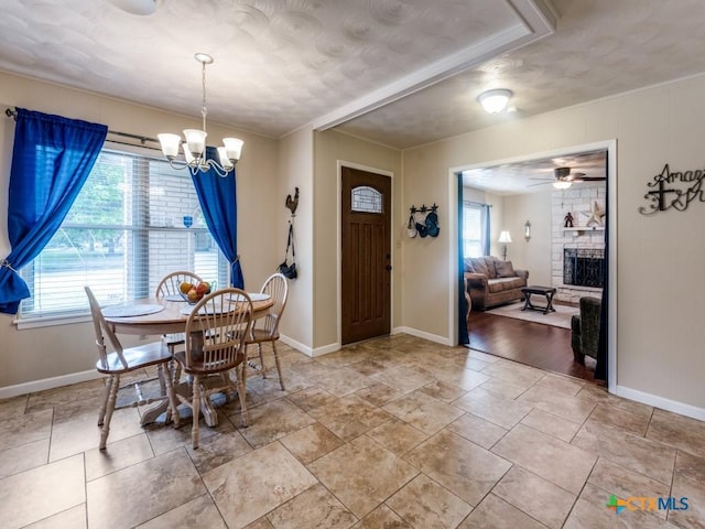 dining area featuring baseboards, a chandelier, ornamental molding, a ceiling fan, and a fireplace