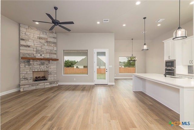 kitchen featuring a stone fireplace, light hardwood / wood-style flooring, hanging light fixtures, white cabinetry, and appliances with stainless steel finishes