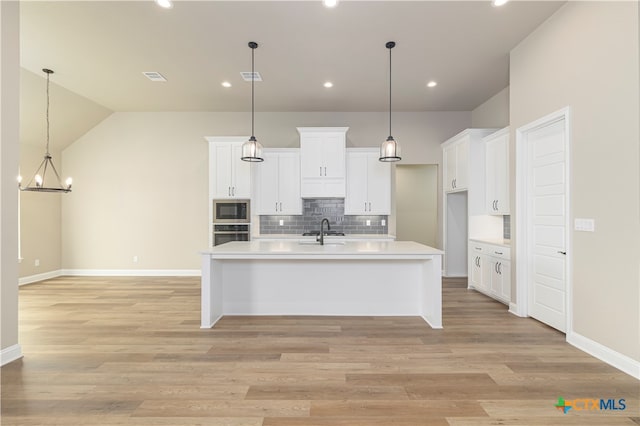 kitchen featuring white cabinetry, sink, appliances with stainless steel finishes, decorative light fixtures, and light hardwood / wood-style flooring