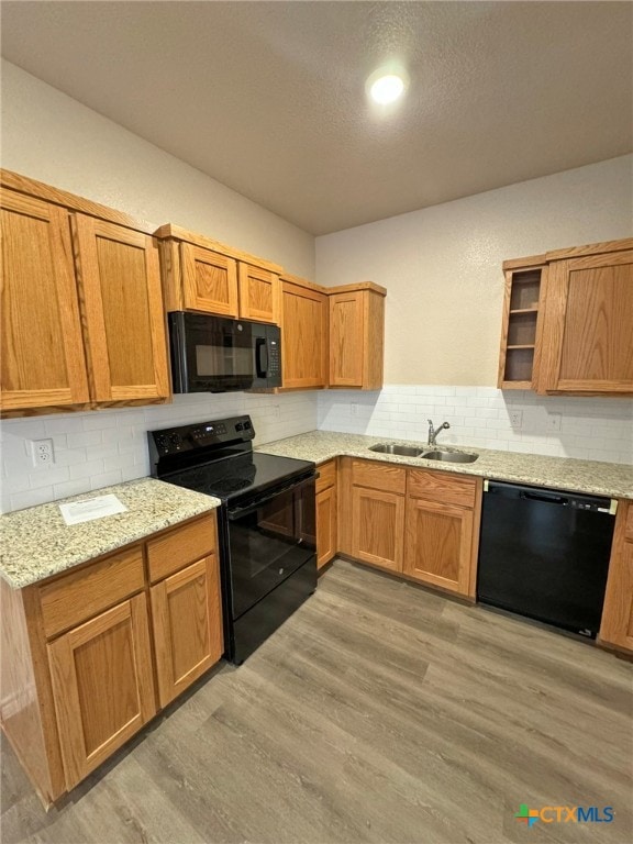 kitchen with backsplash, black appliances, sink, light stone countertops, and light hardwood / wood-style floors