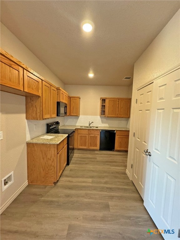 kitchen featuring light stone counters, a textured ceiling, sink, black appliances, and hardwood / wood-style flooring