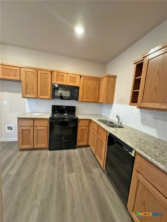 kitchen with backsplash, black appliances, sink, light hardwood / wood-style flooring, and light stone counters