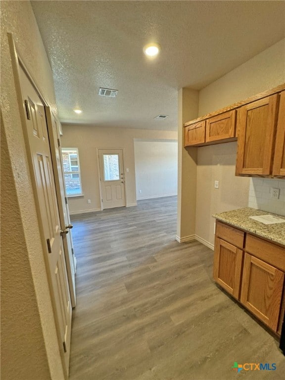 kitchen with backsplash, light stone counters, light hardwood / wood-style floors, and a textured ceiling