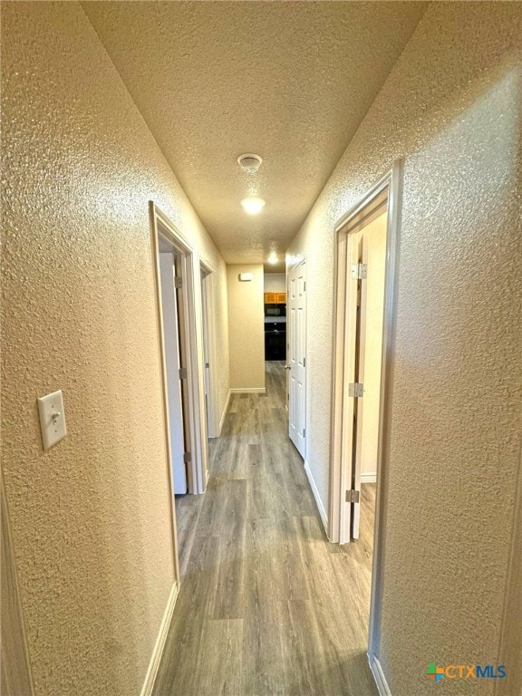 corridor with light hardwood / wood-style floors and a textured ceiling