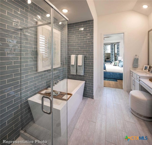 bathroom featuring tile walls, vanity, independent shower and bath, vaulted ceiling, and hardwood / wood-style flooring