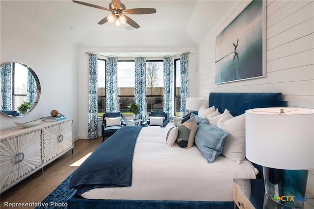 bedroom with hardwood / wood-style floors, ceiling fan, and wooden walls