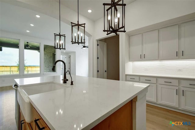 kitchen with white cabinetry, light stone counters, hanging light fixtures, a kitchen island with sink, and light hardwood / wood-style flooring